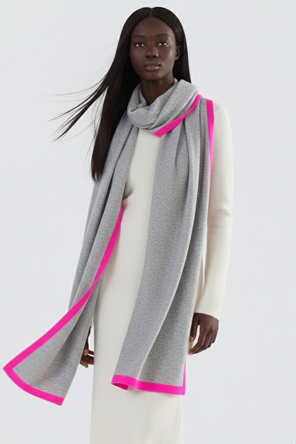 Women's grey cashmere scarf featuring a bright pink border, styled on a female model wearing a matching ivory cashmere sweater and pants. Ideal for cold weather fashion